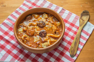 tripe casserole, typical Madrid dish, and wooden spoon on checkered tablecloth, isolated on wooden table