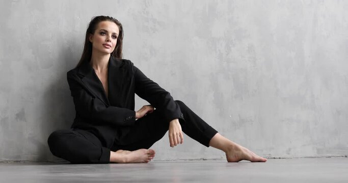 girl model in a black suit posing on a background of gray wall
