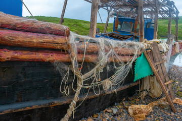 Old abandoned wooden fishing boat in blue color on the beach. A fishing net hangs from the sides.