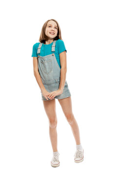 A teenager girl in denim overalls and a blue tank top emotionally jumps up. Isolated on a white background. Vertical.