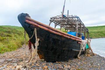 Old abandoned wooden fishing boat in blue color on the beach. A fishing net hangs from the sides