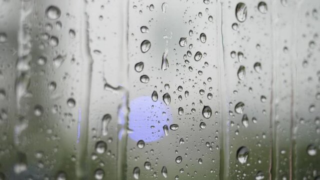 Rain drops on window glass with blur background. A close up of water on glass with the water beading up and running down the glass surface.