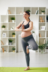 Fototapeta na wymiar Happy young pregnant sportswoman standing on one leg on mat