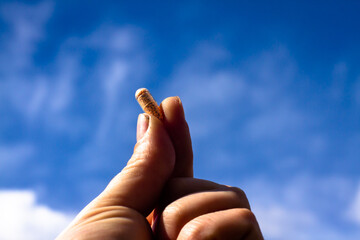 A transparent vitamin tablet or pill held in a hand in front of a cloudy sky