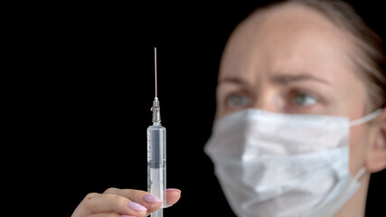 A syringe with a medicine vaccine close up in the hands of female doctor in white medical gown with sterile face mask on black background. Anti virus human health concept. Medicine and vaccination. 