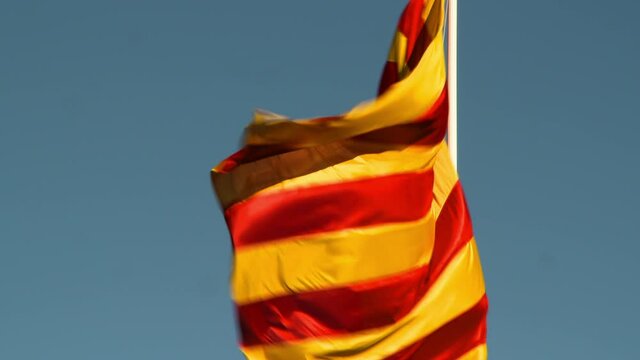 Low angle view of striped flag waving against clear blue sky on sunny day - Girona, Spain