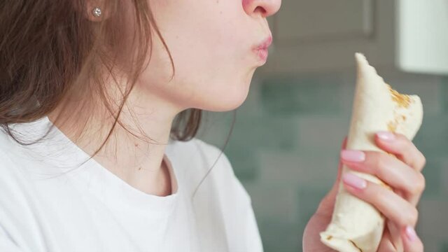 Woman eat kebab. A beautiful girl bites a chicken roll close up. Delicious and harmful fast food