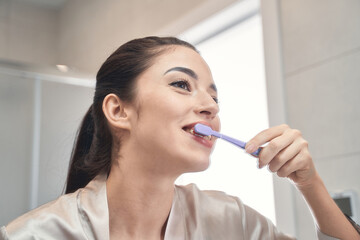 Pleasant young woman cleaning her teeth at bathroom
