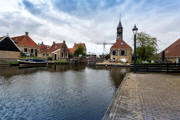 Fototapeta na wymiar The Netherlands - Hindeloopen, a traditional shipping canal ending in a lock. On the right is a church with a wooden tower and a clock, on the left side of the canal are traditional family houses and