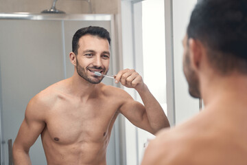 Handsome shirtless man cleaning his teeth at the morning