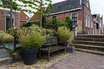 Netherlands - Hindeloopen - a picturesque corner in front of a house with an old wooden bench overgrown with green flowers. In the background brick houses and a path.