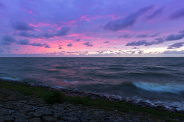 Fototapeta premium Holland - Sunset over the stormy sea. A stone rampart jutting out into the sea. in the foreground sand and green grass.