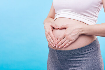 Midsection of young pregnant woman keeping her hands on belly