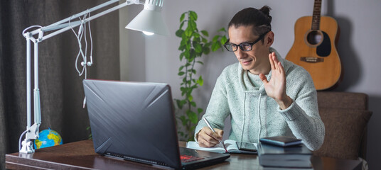 Male student is studying in an online lesson using a laptop at night in the room. Distance...