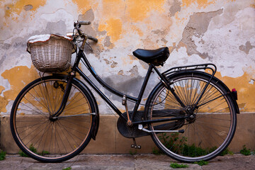 An old bicycle with wicker basket rests against a weathered wall in Lucca, Italy