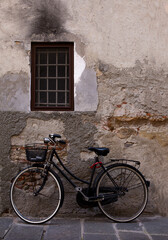 Fototapeta na wymiar An old bicycle with metal basket rests against a weathered cement wall in Lucca, Italy