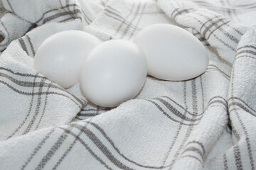 Several huge white chicken eggs on a white checked kitchen towel.