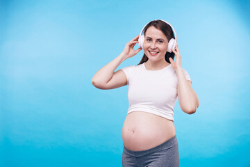 Young cheerful pregnant female with toothy smile and enjoying her favorite music