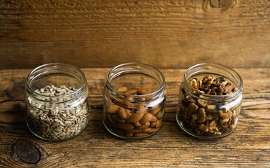 Almond, sunflower seeds and walnut in a small jars which standing on a wooden vintage table. Nuts is a healthy vegetarian protein and nutritious food. Nuts on rustic old wood.