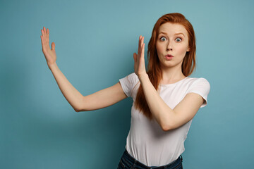 A red-haired girl in a white T-shirt stands and shows with hands a piece from scratch, eyes wide...