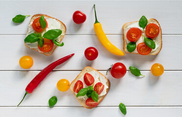 A layout of bruschetta with cheese and cherry and many multicolored tomatoes and peppers and basil leaves