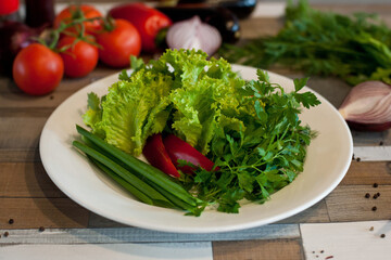 assorted fresh dill, parsley, onion and pepper on a white plate on a wooden table. Vegetarian food