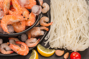 Tiger prawnswith ice cubes in black plate, rice noodles. Tomatoes, garlic cloves, tomato sauce