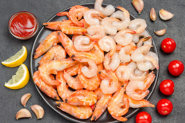 Tiger prawns and shrimp in black bowl. Tomatoes, garlic cloves lemon on table.