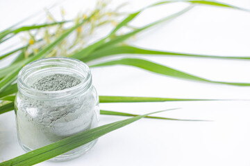 Green clay in a glass jar on a white table with green grass. Spa and body care concept.