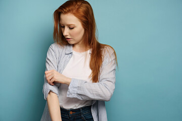 Beautiful red-haired girl in a striped shirt stands on a blue background, rolling up his sleeve