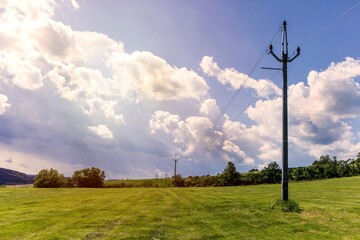 Fototapeta na wymiar Power lines in the countryside against blue sky in summer day. The landscape of the Czech countryside. Energy distribution.
