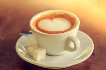 White cup of coffee on a wooden table. Selective focus on foreground