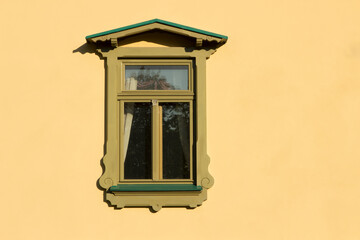 Beautiful carved wooden green window in Russian or Slavic style. Window on the yellow plastered...