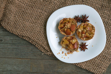 Crispy small tartlets made from shortcrust pastry with apples, homemade sweets with anise and cinnamon. Top view, gunny on a wooden background. Natural eco sweets concept, warm cozy tea party