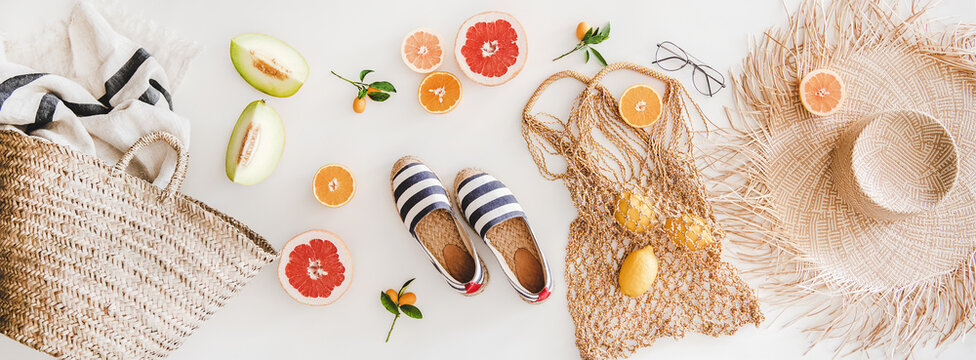 Summer mood layout. Flat-lay of summer natural espadrillas, straw sunhat, beach rafia and net bag, beach towel, sunglasses and fresh fruit over white plain background, top view