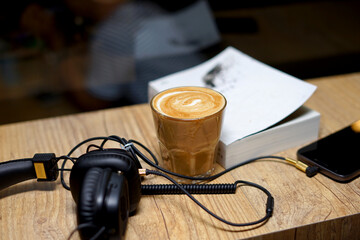 Smartphone, headphones and book on wooden table with coffee latte at Coffee Shop