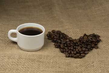 Heart shape made from coffee beans with a spoon and cup of coffee on hessian spelling I love coffee