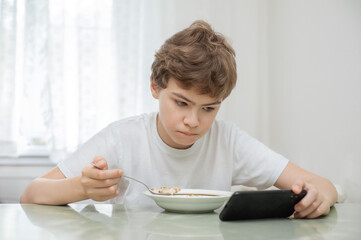 The teenager is having breakfast. He's holding his phone while he's eating.