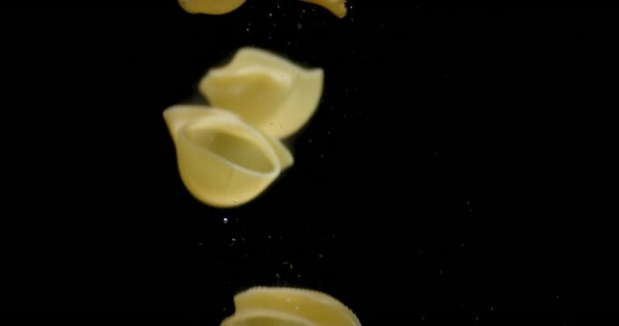 Dry pasta rigati falls under water with air bubbles.