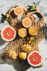 Fototapeta na wymiar Flat-lay of summer natural net bag with various fresh ripe citrus fruits over grey marble background, top view, close-up. Summer organic clean eating food concept