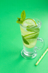 Infused water or cold lemonade with lime, ice and  mint  in the glass  on the green background. Location vertical. Copy space.