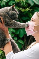 Vertical close-up portrait happy beautiful young woman with cat touching her pink face mask. Green...