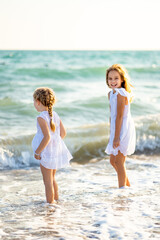 kids, girls walking on beach with big waves in windy weather. vacation to sea. 