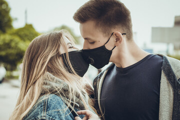 Young couple kissing in protective black masks. Pandemic. Coronavirus. A guy and a girl kiss through a medical mask. Covid 19. Summer 2020.  Kiss.