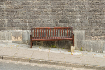 Urban street scene of a wooden bench seat, levelled to compensate for steep incline. Brick wall...