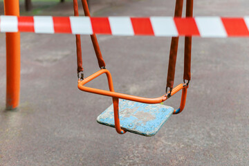 Children's swing on a playground in a recreation park wrapped with red barrier tape. Prohibition of...