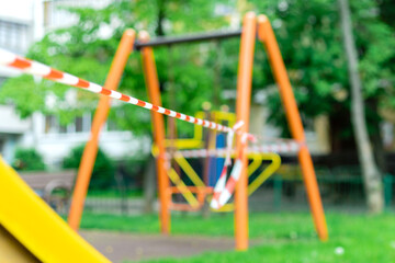 Fototapeta premium Children's playground on the green grass in the park wrapped with red barrier tape. Outside. Prohibition of outdoor walks, prevention of the coronavirus influenza virus covid-19. selective focus