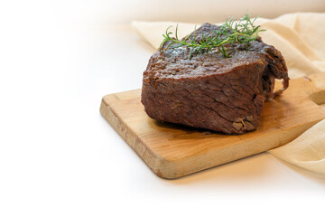 Piece of roast beef braised in red wine with thyme garnish on a cutting board, typical preparation for boeuf bourguignon, the light background is fading to white, copy space