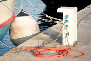 Electrical and water supply pedestal on a pier with hose and cable and a rope on the dock fastened...