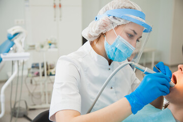 Female dentist curing teeth cavity in blue gloves and protective mask. Dentist caries treatment at...